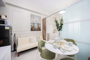 Una habitación moderna con una mesa de comedor, sillas, un sofá, un refrigerador, un microondas, una aspiradora y un cuadro en la pared.