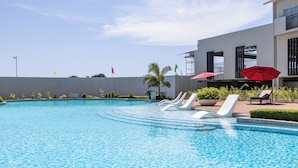 A swimming pool with lounge chairs and umbrellas, surrounded by a building with a white exterior and a grey fence. - Modern Nordic Studio with Balcony and Pool in Primeworld District Near Airport (Lapu-Lapu)
