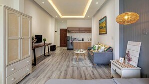 Una sala de estar moderna con un sofá, una mesa de centro y un televisor. Se ve una cocina al fondo con gabinetes de madera y un refrigerador.