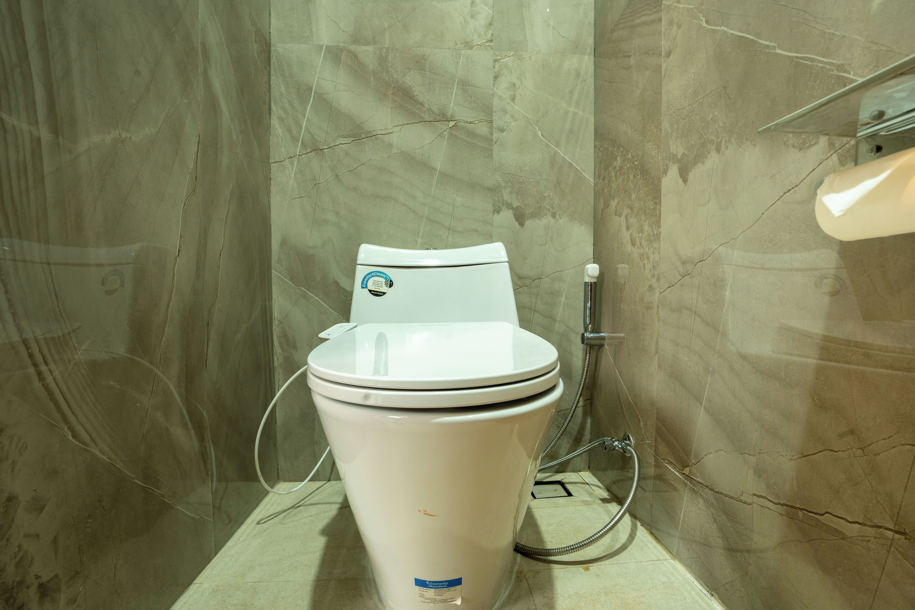 A modern bathroom with a white toilet, marble walls, and a shower area.