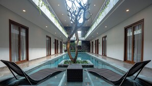 Un área de piscina con sillas de descanso, un árbol central y una pared de piedra.