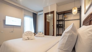 Una habitación de hotel con una cama, televisión, armario y una lámpara colgante.