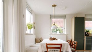 A dining area with a table set for four, a bench, and a kitchen area with cabinets and a refrigerator. - Nice holiday home on the water in Grou (Grou)