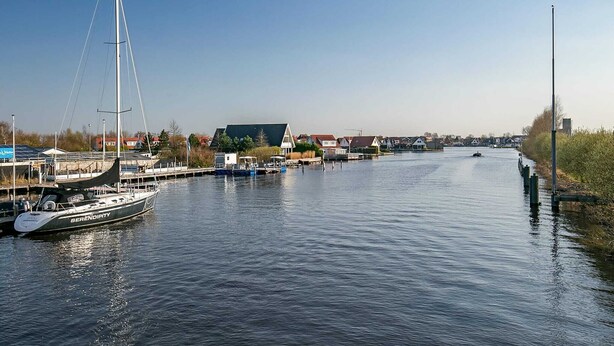 A river with a sailboat docked on the left and a building with a sloped roof in the background. - Nice holiday home on the water in Grou (Grou)