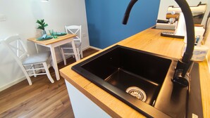 A kitchen with a black sink, a wooden countertop, a white chair, a small table, and a hanging light fixture.