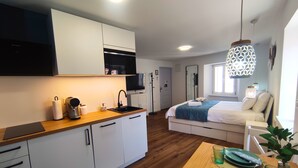 A modern kitchen with white cabinets, a wooden countertop, and a built-in microwave. There is a dining area with a table set for two, a green vase, and a plant.