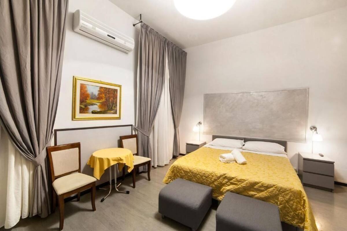 A hotel room with a bed, a desk, a chair, a table, and a painting on the wall.