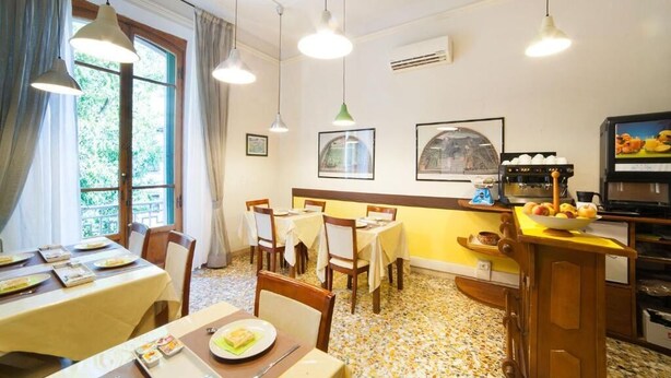 A dining area with tables set for meals, a kitchen area with appliances, and a window with curtains. - BB Melody House (Florence)