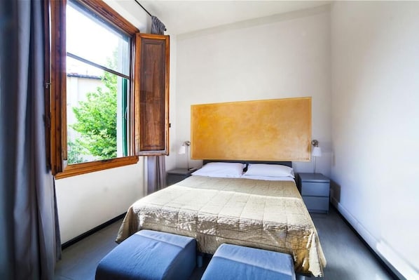 A bedroom with a large bed, a nightstand, a window with curtains, and a view of greenery outside. - BB Melody House (Florence)