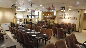 A spacious dining area with multiple tables and chairs, a buffet setup, and a 'Happy Anniversary' decoration on the wall.
