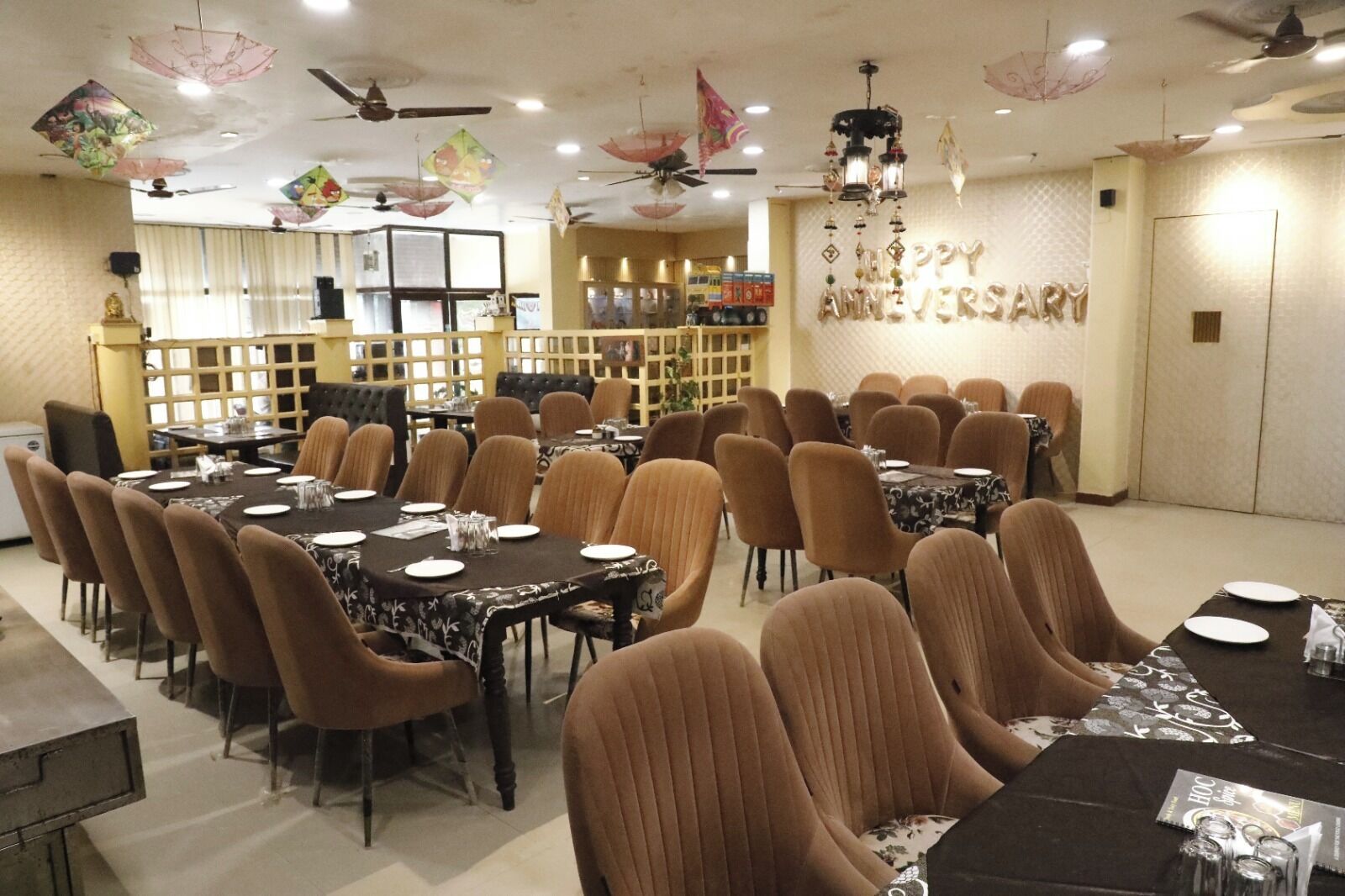 A dining area with multiple tables and chairs, ceiling fans, and decorative umbrellas.