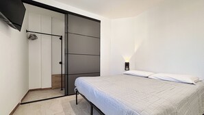 A bedroom with a bed, a wardrobe, and a nightstand with a lamp. - Tiny Loft Skydeck (Civitavecchia)