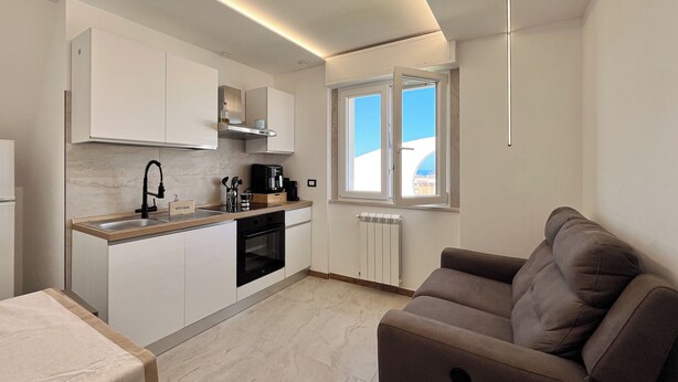 A modern kitchen with white cabinets, a built-in oven, and a window with a view of the sky. - Tiny Loft Skydeck (Civitavecchia)