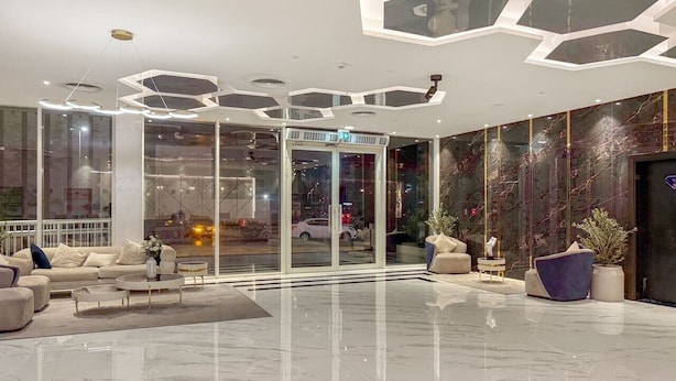 En moderne lobby med glasklædt indgang, siddeområde med sofaer og sofabord, samt et dekorativt loft med geometriske mønstre.