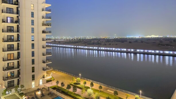 A high-rise hotel with balconies overlooking a calm river, a pool, and a well-lit promenade. - FIRST CLASS | 1BR | Tranquility in Style (Abu Dhabi)