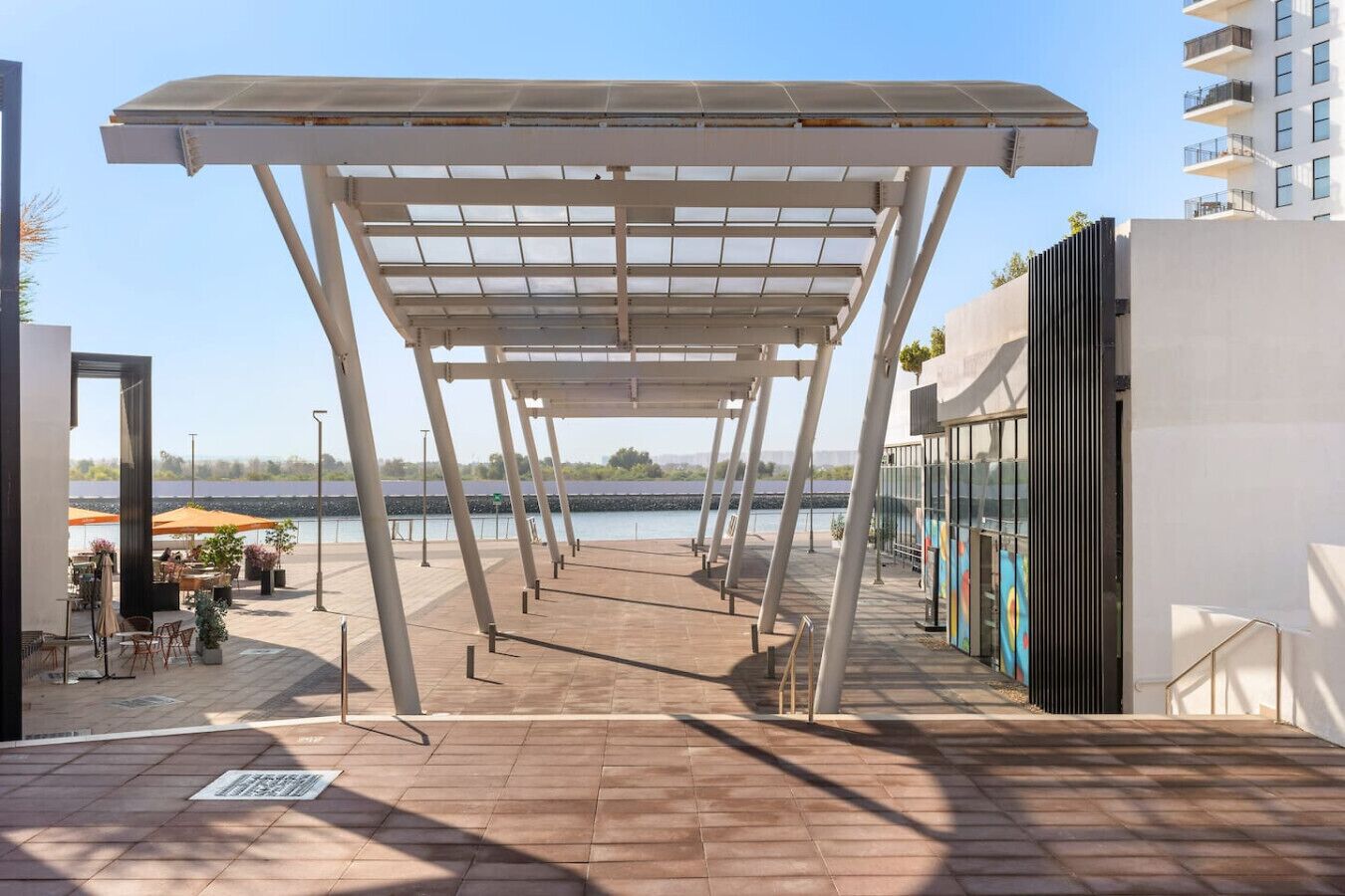 An outdoor patio area with a pergola structure, a seating area with tables and chairs, and a view of a body of water.
