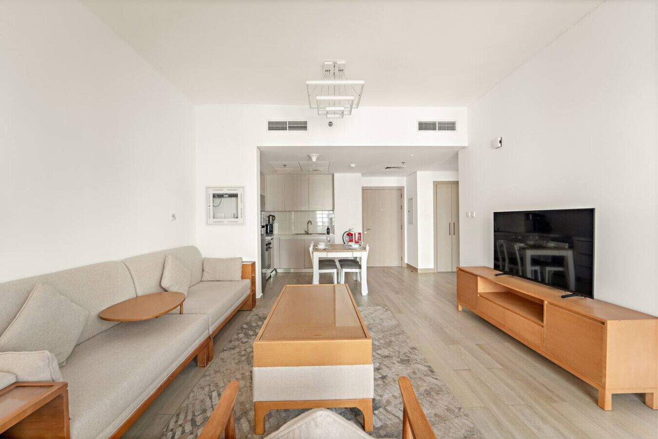 Una sala de estar moderna con un sofá, una mesa de centro, un mueble para la televisión y una cocina al fondo.