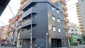 A multi-story building with a dark facade, multiple balconies, and a bicycle parked in front. - XS42 XROSS STAY Juso2 (大阪市淀川区十三東)