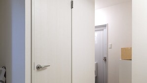 A hallway with a wooden herringbone floor, a white door with a silver handle, and a light switch on the wall. - XS42 XROSS STAY Juso2 (大阪市淀川区十三東)