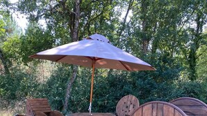 A rustic outdoor seating area with wooden barrels as chairs and a table, surrounded by trees. - Relaxation tent (Callen)