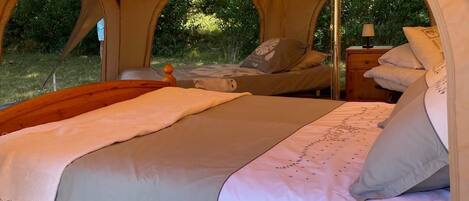 A tent with two beds, each with pillows and blankets, and a small table with a lamp.