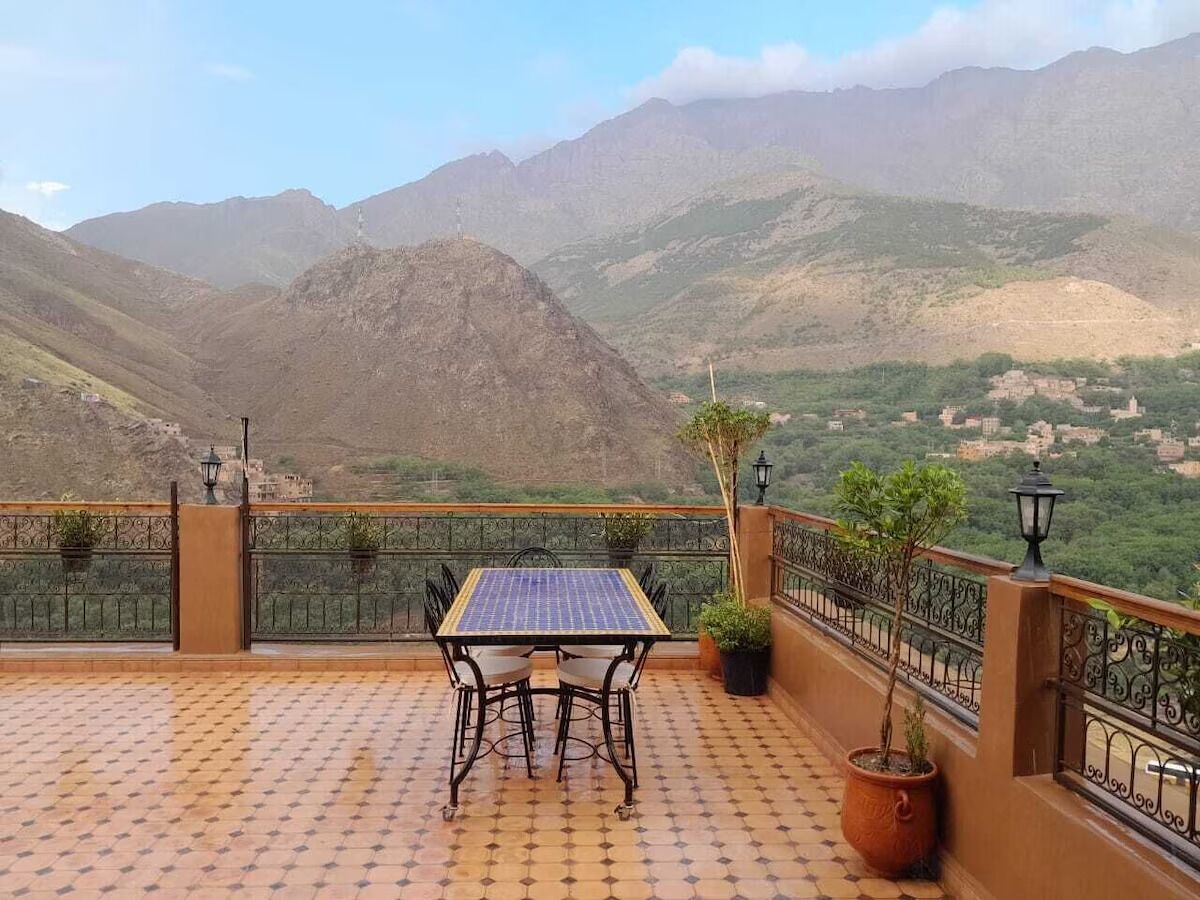 Una terraza con mesa y sillas, plantas en macetas y vistas a las montañas.