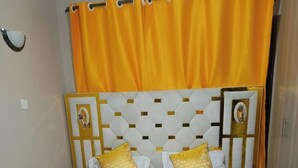 Un lit recouvert d’une couvre-lit blanche et dorée, une tête de lit ornée d’un motif géométrique et deux appliques murales.