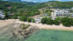 An aerial view of a coastal area with a sandy beach, clear water, and a mix of residential buildings and greenery. - VIP Dream Suite Residence Krabi (Krabi)