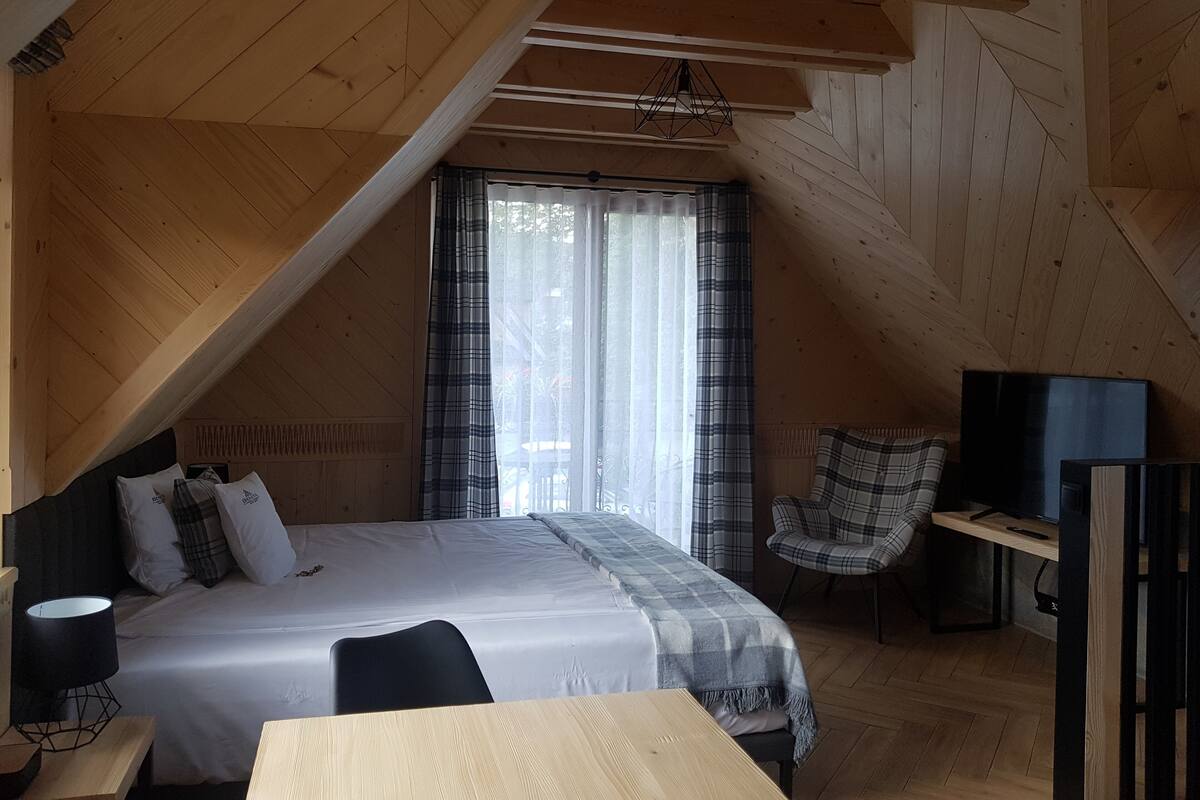 A bedroom with a bed, a chair, a desk, and a window with curtains.