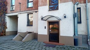 A building with a brown and white facade, a small entrance with a glass door, and a window with a view of trees.