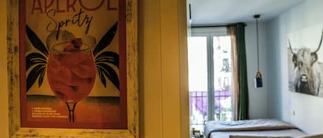 Una habitación con una cama, un cartel enmarcado en la pared y una ventana con cortinas.
