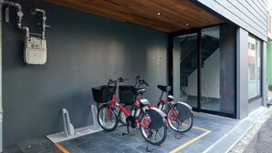 Un edificio moderno con fachada gris, techo de madera y entrada de vidrio. Dos bicicletas rojas están estacionadas afuera, cada una con una cesta y un candado.