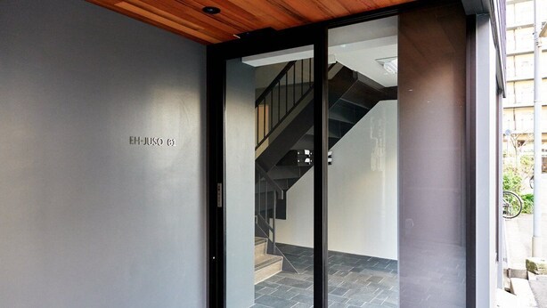 Una entrada moderna con puerta de vidrio, techo de madera y una escalera visible a través del cristal.