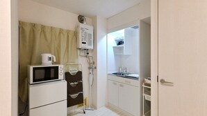 Una kitchenette compacta con microondas, calentador de agua y lavamanos.