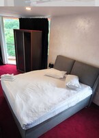 Una cama grande con ropa blanca, un cabecero gris y una alfombra roja.