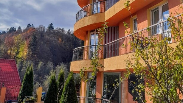 A multi-story building with balconies, a red roof, and a garden area with trees and shrubs. - Pensiunea Lucy Sinaia (Sinaia)
