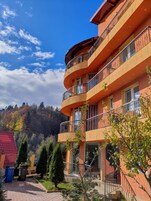 Un edificio de varios pisos con balcones, techo rojo y un jardín con árboles y arbustos.