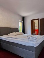 Una habitación de hotel moderna con una cama grande, una ventana con cortinas y una puerta que conduce a un baño.