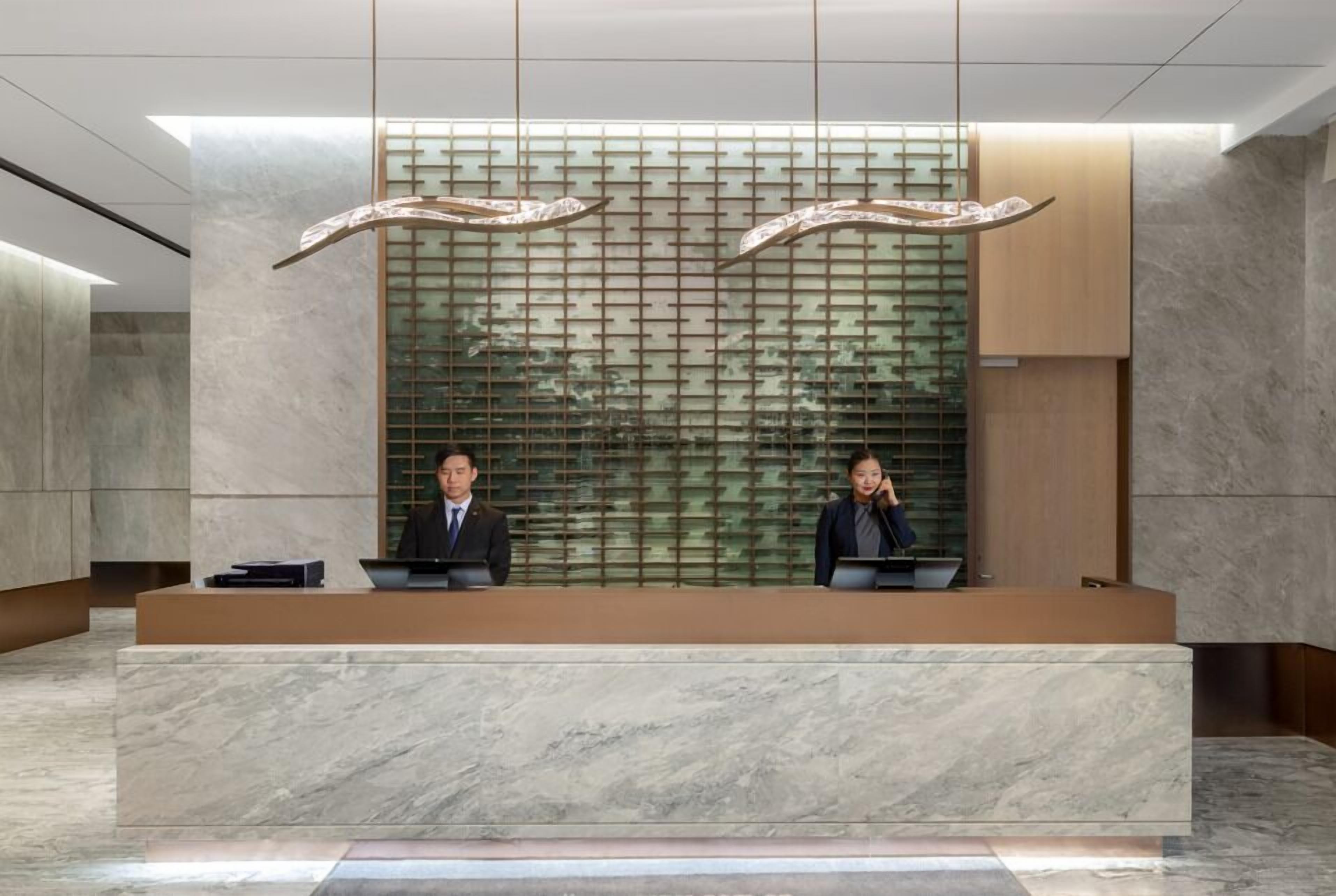 A reception desk with two staff members, a modern interior with a marble floor, and a decorative wall with a grid pattern.