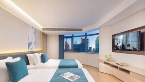Ein modernes Hotelzimmer mit zwei Betten, einem großen Fenster mit Blick auf die Stadt, einem Flachbildfernseher und einer kleinen Schreibtischzeile.