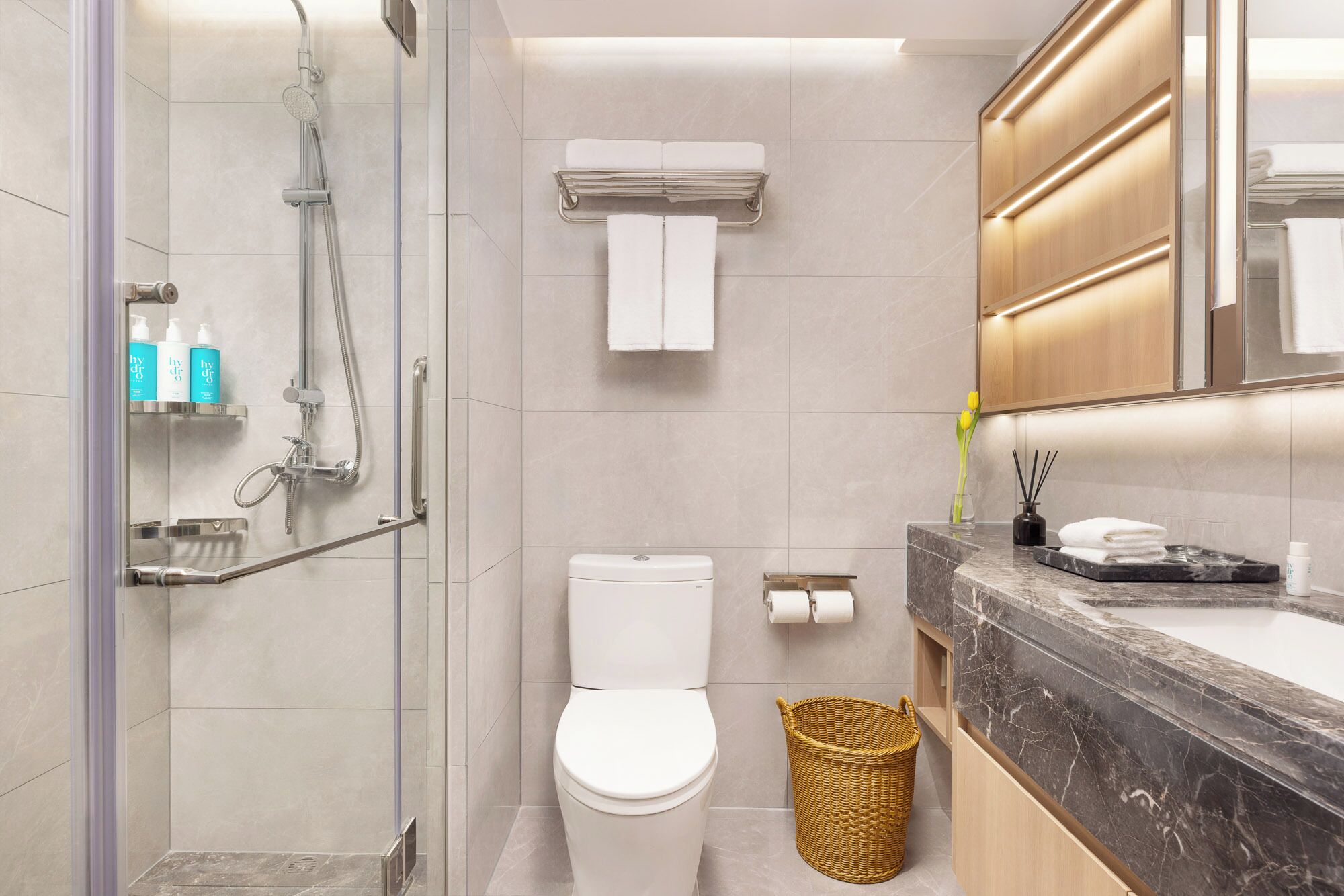 Une salle de bain moderne dotée d’une douche à parois de verre, de toilettes, d’un lavabo en marbre et d’un miroir avec éclairage intégré.