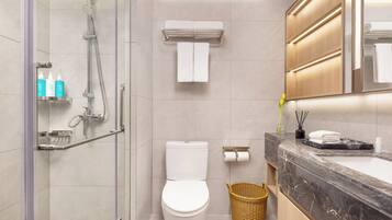 A modern bathroom with a glass-enclosed shower, a toilet, a marble sink, and a mirror with integrated lighting.