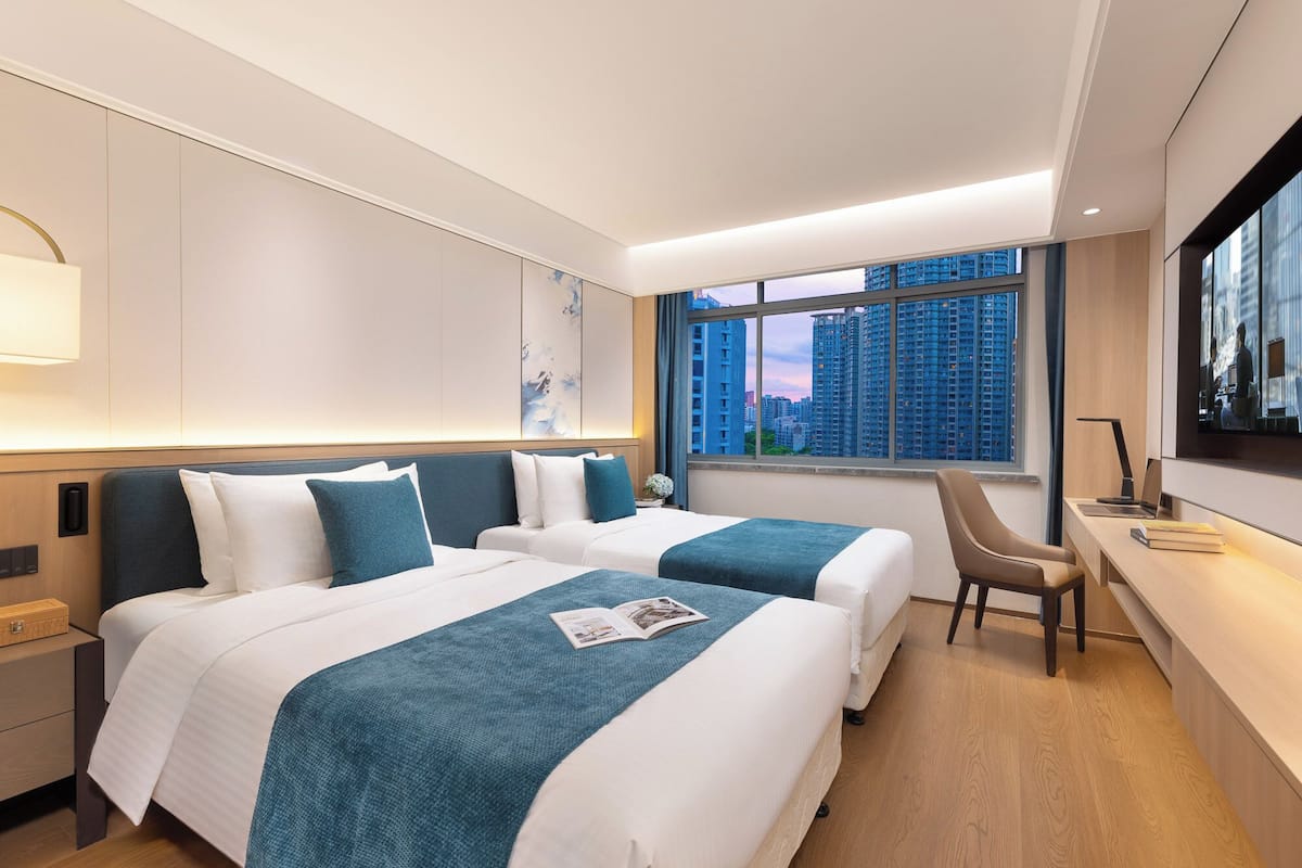 Une chambre d’hôtel avec deux lits, un bureau, une chaise et une grande fenêtre donnant sur la ville.