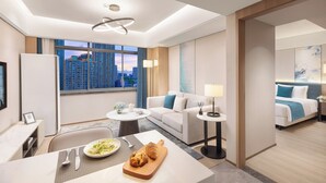 Ein modernes Hotelzimmer mit Blick auf die Stadt, einem Essbereich, einer Couch, einem Bett und einem kleinen Tisch mit einer Teller Essen.