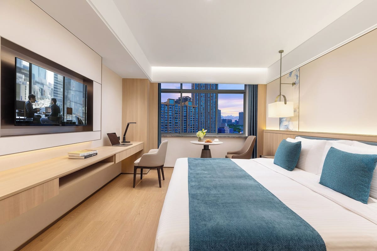 Une chambre d’hôtel moderne dotée d’un grand lit, d’un bureau, d’une chaise, d’une télévision et d’une fenêtre donnant sur la ville.