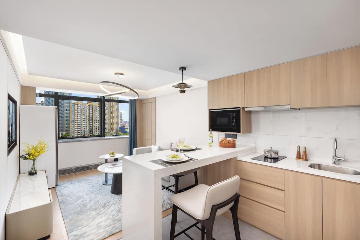 Une cuisine moderne dotée d’un îlot central, de meubles en bois, d’un four à micro-ondes encastré et d’une grande fenêtre offrant une vue sur la ville.