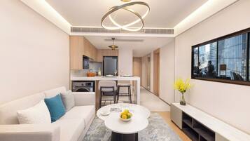A modern living room with a sofa, a coffee table with fruit, a TV, and a kitchen in the background.