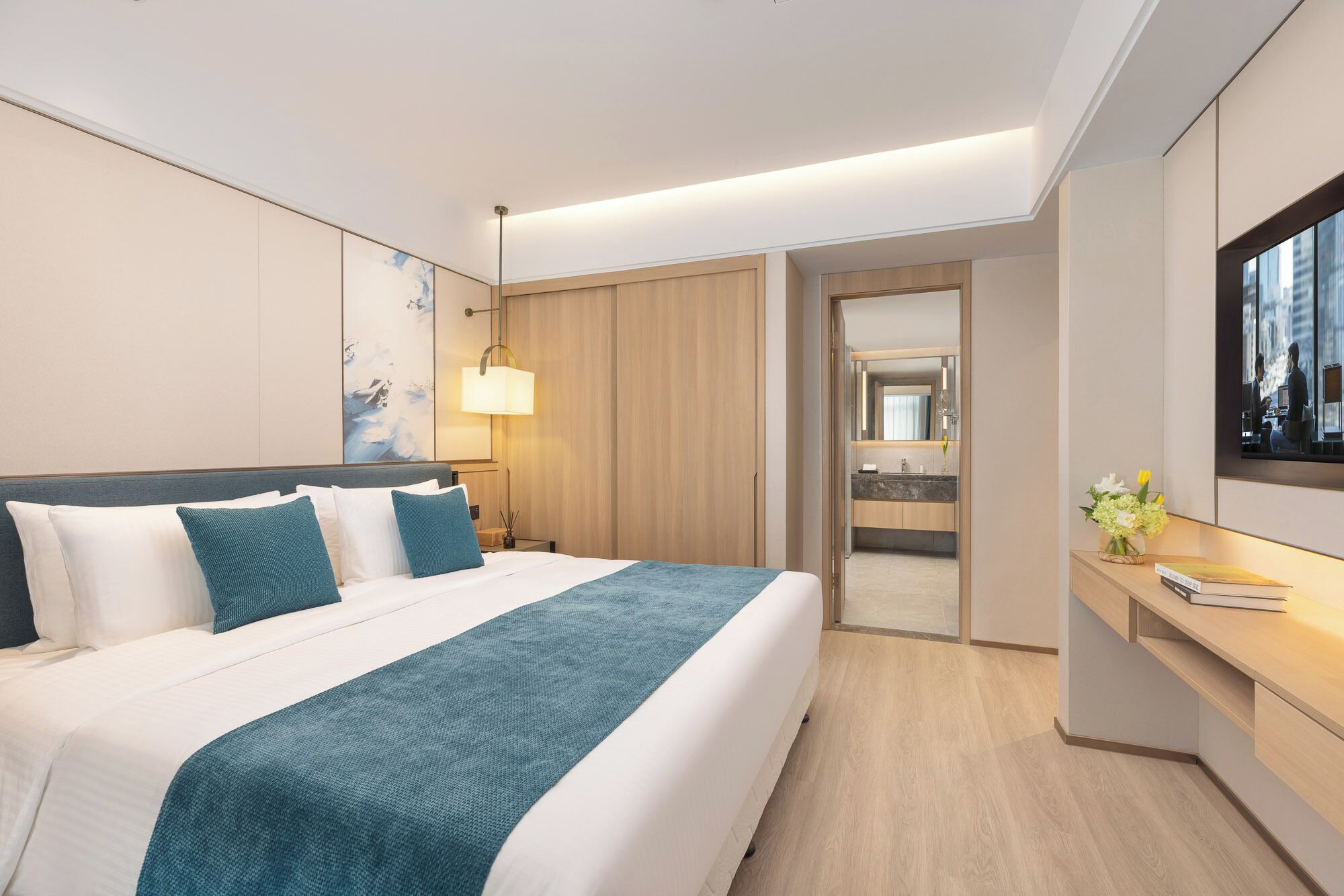 Una habitación de hotel moderna con una cama grande, un escritorio, un televisor y un baño visible a través de una puerta abierta.