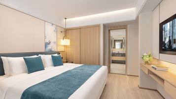 Una habitación de hotel moderna con una cama grande, un escritorio, un televisor y un baño visible a través de una puerta abierta.