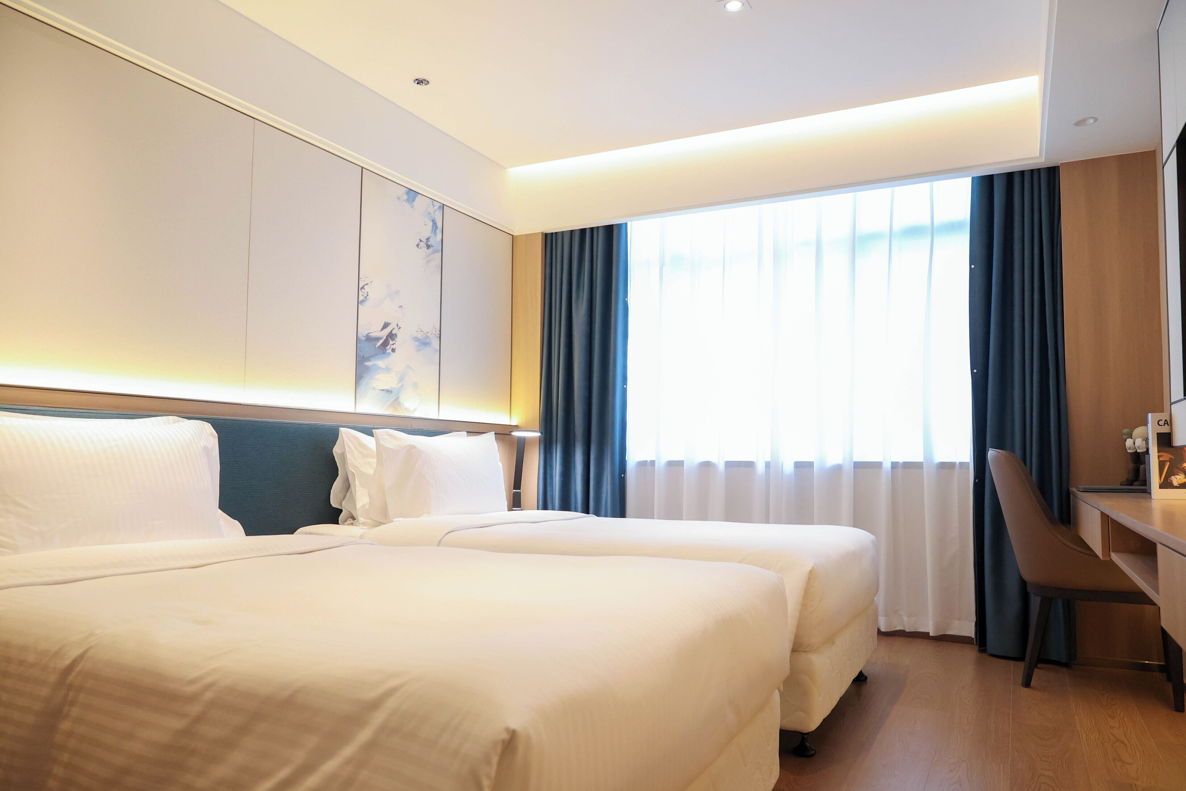 Una habitación de hotel con dos camas, un escritorio y un ventanal grande con cortinas.